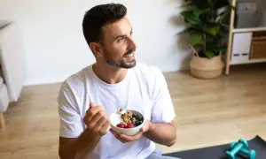 Un jeune intermittent savoure un bol de yaourt grec avec des fruits rouges et du granola, prêt pour sa journée.
