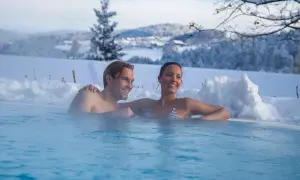 Ein Paar entspannt in einem beheizten Pool im Schnee mit verschneiter Landschaft im Hintergrund.