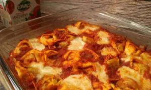 Pyszna zapiekanka z tortellini w sosie pomidorowym, zapieczona z serem. Obok kartonik przecieru pomidorowego Łowicz.