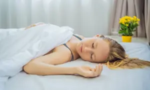 A woman sleeps peacefully on a white bed, her head resting directly on the mattress. Is it better to sleep without a pillow?