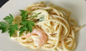 Cremige Pasta al Limone mit Garnelen und Petersilie auf einem weißen Teller. Ein Genuss für Augen und Gaumen.