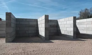 Budowa muru oporowego z bloczków betonowych. Konstrukcja w kształcie litery L, z widocznymi słupkami wzmacniającymi.