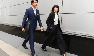 Para idą w eleganckim business attire, mężczyzna w granatowym garniturze, kobieta w czarnym.