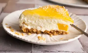 Ein cremiges Stück Kuchen ohne Backen mit gelber Fruchtschicht und knusprigem Boden auf einem Teller.