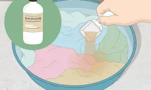 Eine Hand gibt eine Messlöffel-Menge einer Flüssigkeit in eine Schüssel mit bunten Kleidungsstücken und Wasser. Die Flüssigkeit hilft, den **Geruch aus Kleidung entfernen**.