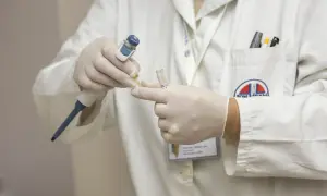 Laborant w białym fartuchu, rękawiczkach i z identyfikatorem przygotowuje próbkę do analizy. To kluczowy etap przed obdukcją.