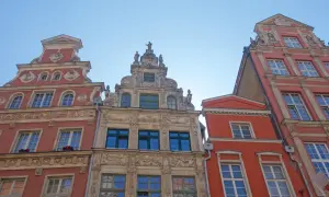 Bogata gdańsk architektura kamienic z detalami rzeźbiarskimi i ozdobnymi fasadami, widziana z dołu pod błękitnym niebem.