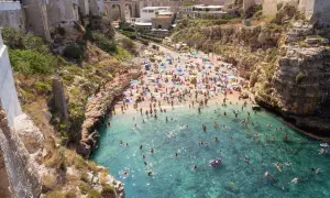 Una spiaggia affollata a Polignano a Mare, Italia, con persone che prendono il sole e nuotano nelle acque cristalline.