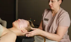 Relaks w gabinecie head spa. Kobieta leży z kamieniami na oczach, a masażystka delikatnie dotyka jej skroni.
