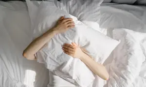 A person clutches a pillow in bed, sunlight dappling the sheets. This scene evokes the struggle many with ADHD face: do people with ADHD have trouble sleeping?