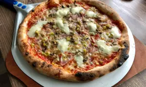 Chrupiąca pizza z pieca kamiennego z serem, pieczarkami i oliwkami na łopacie.