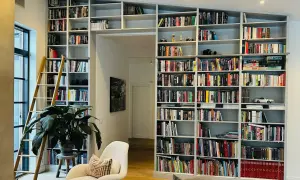 En stor inbyggd bokhylla med en stege, fylld med böcker och prydnadssaker. Perfekt inbyggd bokhylla inspiration för ett bibliotek.