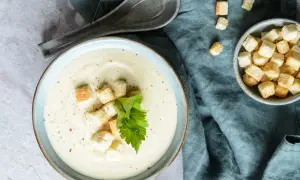 Kremowa zupa z kalarepy z grzankami i natką pietruszki na niebieskim tle.