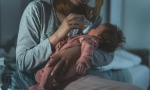 Zmęczona mama karmi butelką niemowlę, które obudziło się w nocy i nie śpi 2 godziny.