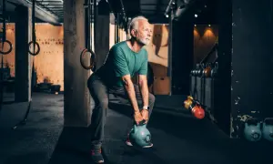 Älterer Mann trainiert mit Kettlebell, stärkt seine bauchmuskeln im Fitnessstudio.