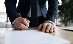 Mężczyzna w garniturze podpisuje dokument, który może być wypowiedzeniem umowy o pracę.