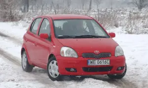 Czerwona Toyota Yaris 1 na śniegu. Kierowca przygotowuje się do wymiany żarówki.