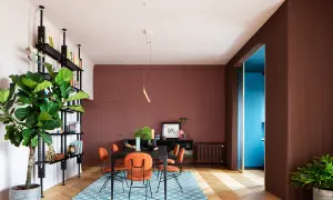 Un soggiorno moderno con pareti color mattone, sedie arancioni vivaci e un tappeto blu. Un esempio di come abbinare il color mattone con tocchi audaci.