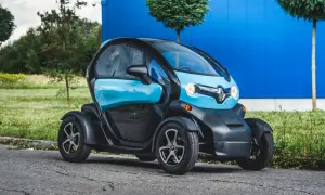Niebiesko-czarny Renault Twizy, mały samochód elektryczny, zaparkowany na tle niebieskiego budynku i zieleni.