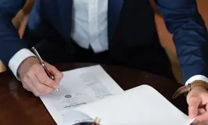 Mężczyzna w garniturze podpisuje dokument, składając oświadczenie woli.