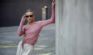 Modelka w różowej bluzce z długim rękawem i szarych spodniach, zastanawia się, jaka bluzka do różowych spodni pasuje najlepiej.