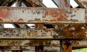 Metalowe belki konstrukcji pokryte rdzą i łuszczącą się farbą. To przykład tego, co to jest korozja, niszcząca metal.