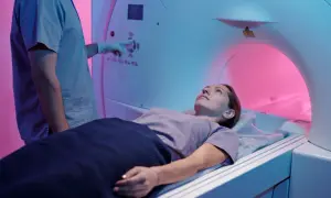 Une femme est allongée dans un appareil de TDM. Le technicien, en blouse bleue, ajuste les commandes. La TDM, c'est quoi ? Un examen d'imagerie médicale.