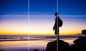 Sylwetka fotografa na tle zachodu słońca, z księżycem na niebie. Kompozycja zgodna z zasadami fotografii, z liniami siatki.