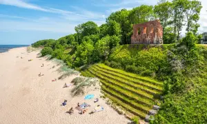 Piękny klif w Trzęsaczu z ruinami kościoła na szczycie. Piaszczysta plaża z wypoczywającymi ludźmi poniżej.