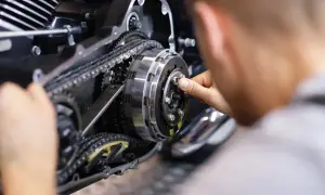 Mechanik naprawia sprzęgło motocykla, widoczny mechanizm z łańcuchem i zębatkami.