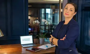 Kobieta w garniturze, z laptopem z napisem "LEADERSHIP DASHBOARD", uczy jak zostać managerem.