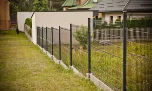 Nowoczesne ogrodzenie ze spadkiem terenu, biegnące wzdłuż trawnika i domów.