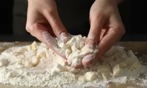 Dłonie przesiewają mąkę krupczatkę, przygotowując ciasto na kruche ciasteczka. Idealna do wypieków.