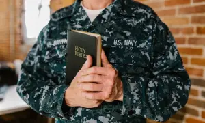 Marynarz w mundurze US Navy trzyma Biblię. W jego dłoniach spoczywa księga, niczym pieśń nad pieśniami, symbol wiary i nadziei.