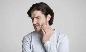 Uomo con mano sulla guancia, espressione di dolore. Potrebbe soffrire di disestesia o parestesia.