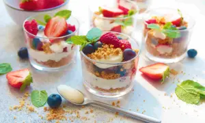 Délicieux **crumble fruits rouges** en verrines, garni de fraises, framboises, myrtilles et menthe. Une cuillère attend patiemment.