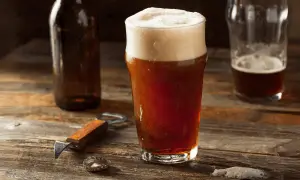 Un bicchiere di birra rossa con schiuma abbondante, accanto a una bottiglia e un apribottiglie. Perfetta per gustare i suoi gradi.