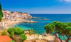 Vue pittoresque d'une crique ensoleillée avec des maisons blanches, des bateaux colorés et des eaux turquoises, parfait pour les activités Costa Brava.
