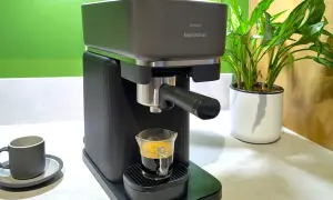 En Philips Baristina espressomaskin brygger en perfekt shot kaffe till espressomaskin. En grön vägg och en krukväxt i bakgrunden.