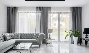 Elegancka szara sofa z pikowanymi poduchami i kryształkami, szklany stolik i dywan tworzą wnętrze w **stylu glam**.
