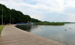 Drewniana promenada nad jeziorem, z widokiem na trzciny i pływające kaczki. Dąbki atrakcje dla miłośników natury i spokoju.