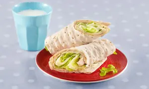 Två saftiga tonfisk wraps med krispig sallad på en röd tallrik, bredvid ett glas mjölk.