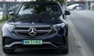 Ciemnoniebieski Mercedes EQC z tablicą rejestracyjną WW 514SE zaparkowany przy ulicy, w tle most.