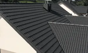 Szare, nowoczesne dachy betonowe pokrywają domy na tle zielonych wzgórz.