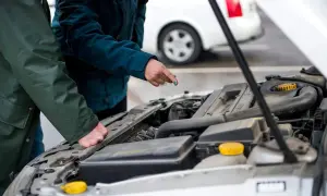 Två personer inspekterar en bilmotor. En person pekar på något i motorn, kanske för att förklara något om service på bilen.