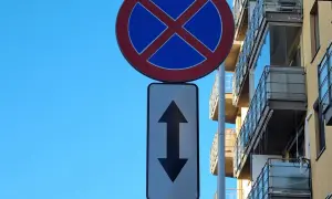 Znak zakaz postoju z tabliczką wskazującą, że zakaz obowiązuje na obu kierunkach. Budynek z balkonami w tle.