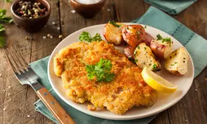 Goldbraunes Schnitzel, perfekt paniert, mit Rosmarinkartoffeln und Zitrone. So paniert man Schnitzel für ein köstliches Essen.