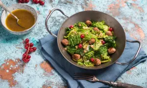 Wirsingsalat mit Fleischbällchen und roten Johannisbeeren in einer Metallschüssel, daneben eine Schüssel mit Dressing.