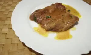 Due fettine di tacchino appetitose, immerse in una salsa dorata e profumata, servite su un piatto bianco.