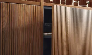 Rillenfronten aus dunklem Holz, die eine Tür eines Schranks bilden. Darin ein Buch und eine schwarze Box.